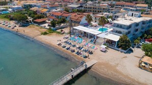 An aerial view of a coastal town with a beach, a swimming pool, and a pier.