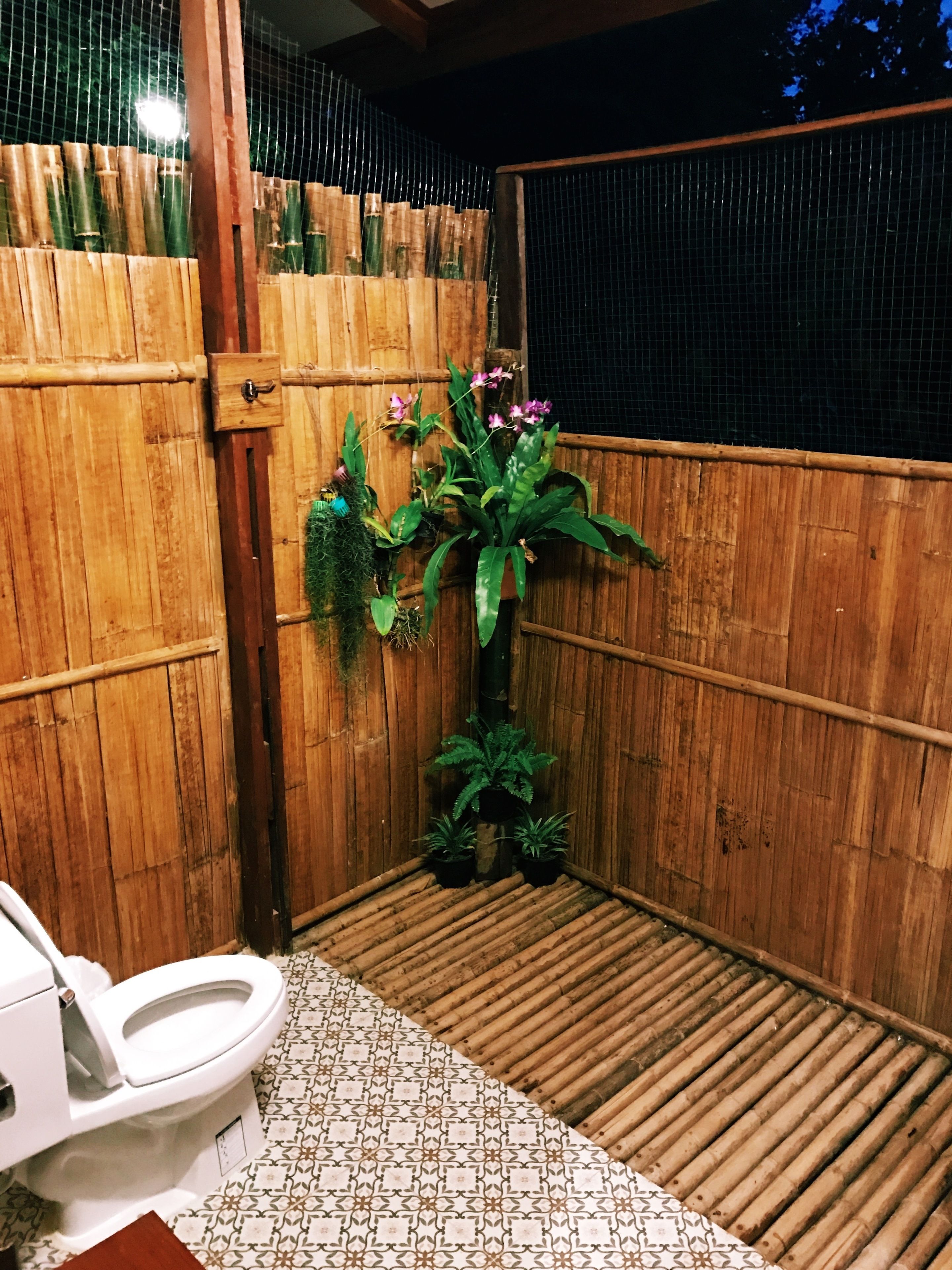 Baño con inodoro, pared de bambú y plantas en macetas.