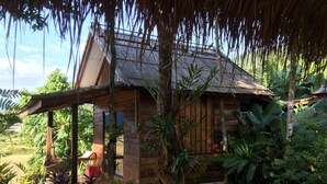 Una cabaña de madera con techo de paja, rodeada de exuberante vegetación tropical.