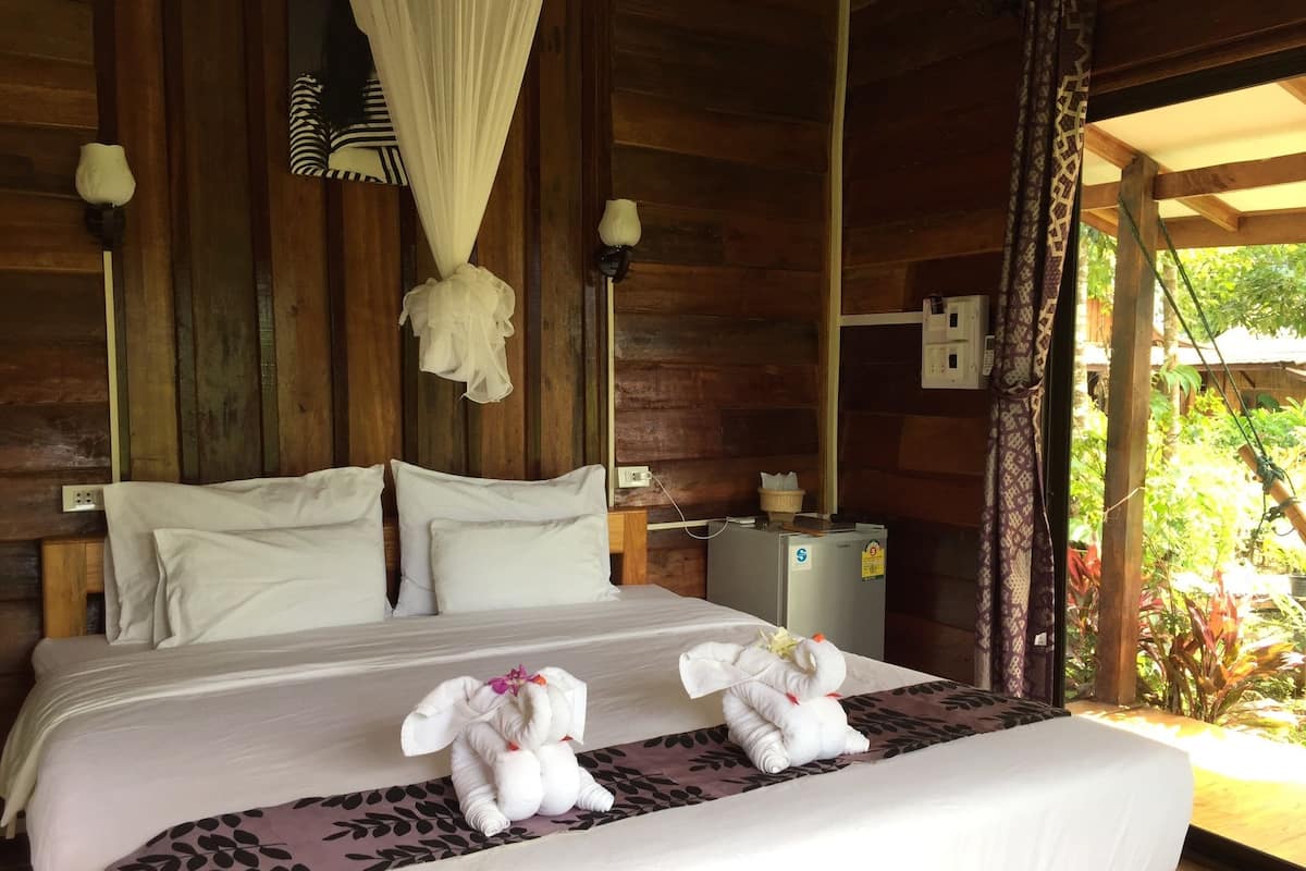 Una habitación tipo cabaña de madera con una cama, dos toallas con forma de animales y un refrigerador pequeño.