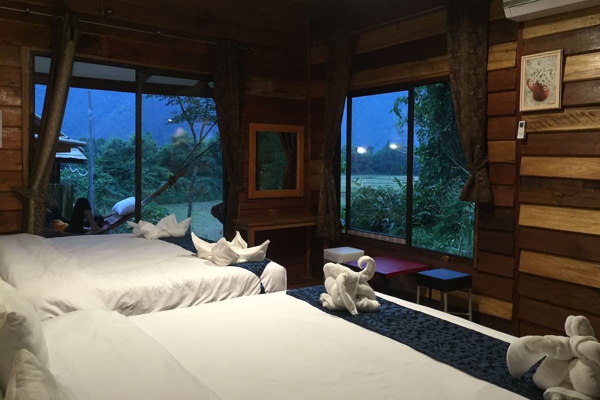 Habitación de cabaña de madera con dos camas, una mesita y vista a un bosque.