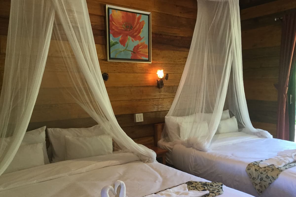 Una habitación con dos camas, cada una con ropa blanca y dosel. Hay un cuadro en la pared sobre las camas.
