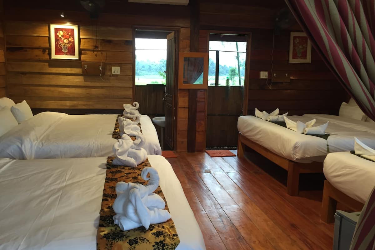 Una habitación tipo cabaña de madera con dos camas, cada una con toallas ordenadas y un corredor de cama estampado con motivos florales.