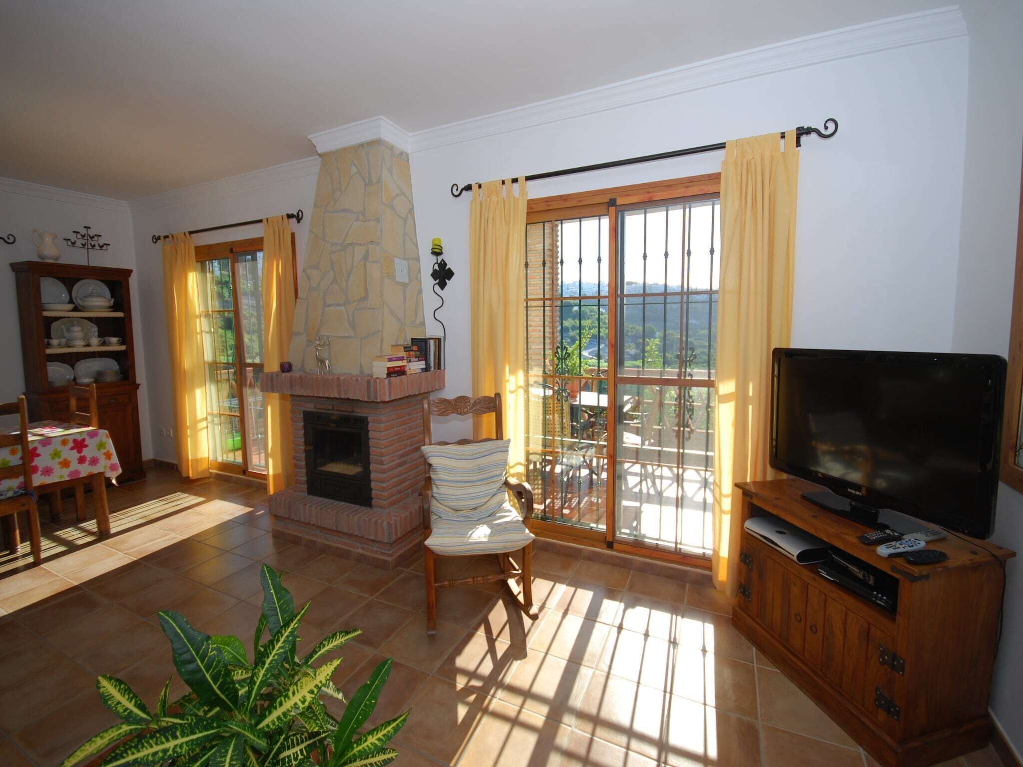A living room with a fireplace, a television, a dining area with a table and chairs, and a balcony with curtains.