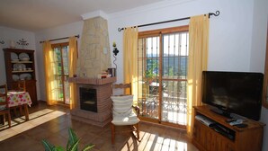 A living room with a fireplace, a television, a dining area with a table and chairs, and a balcony with curtains. - Belvilla by OYO Francisco (Frigiliana)