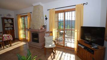 A living room with a fireplace, a television, a dining area with a table and chairs, and a balcony with curtains.