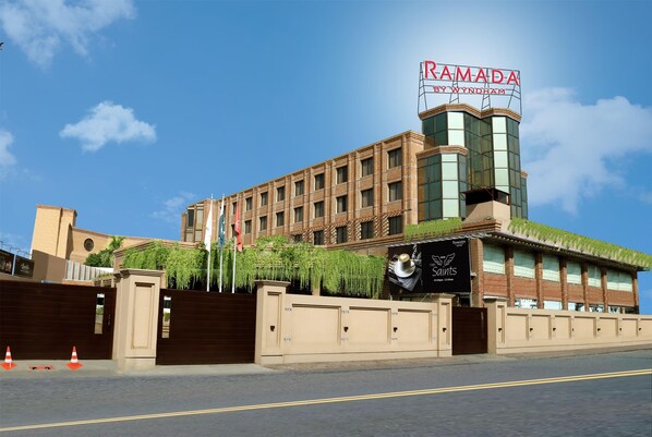 A hotel with a prominent sign reading "RAMADA BY WYNDHAM" and a large glass facade.