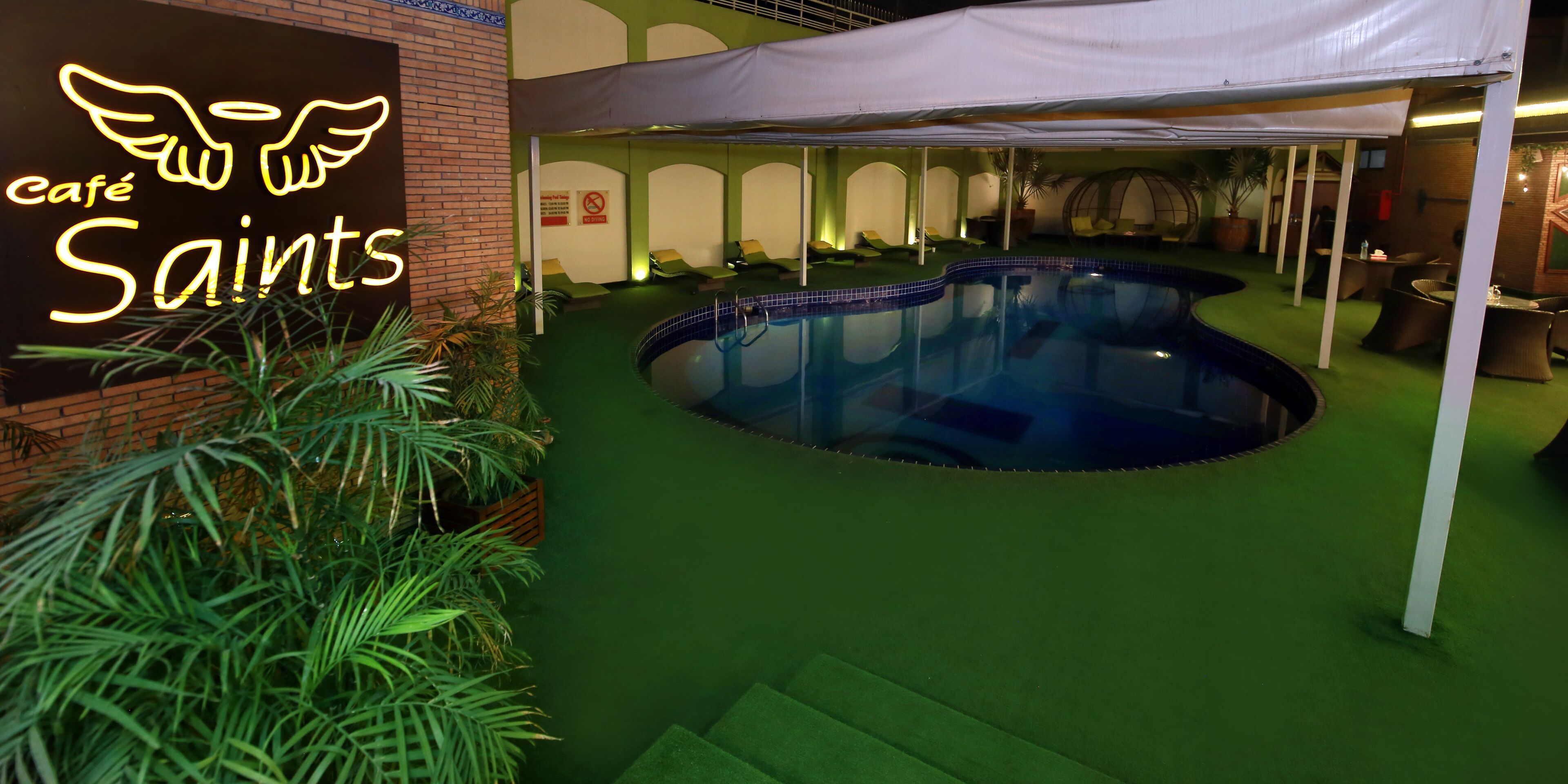 An indoor pool area with a neon sign reading "café Saint's" and a tent structure.