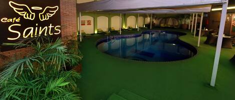An indoor pool area with a neon sign reading "café Saint's" and a tent structure.