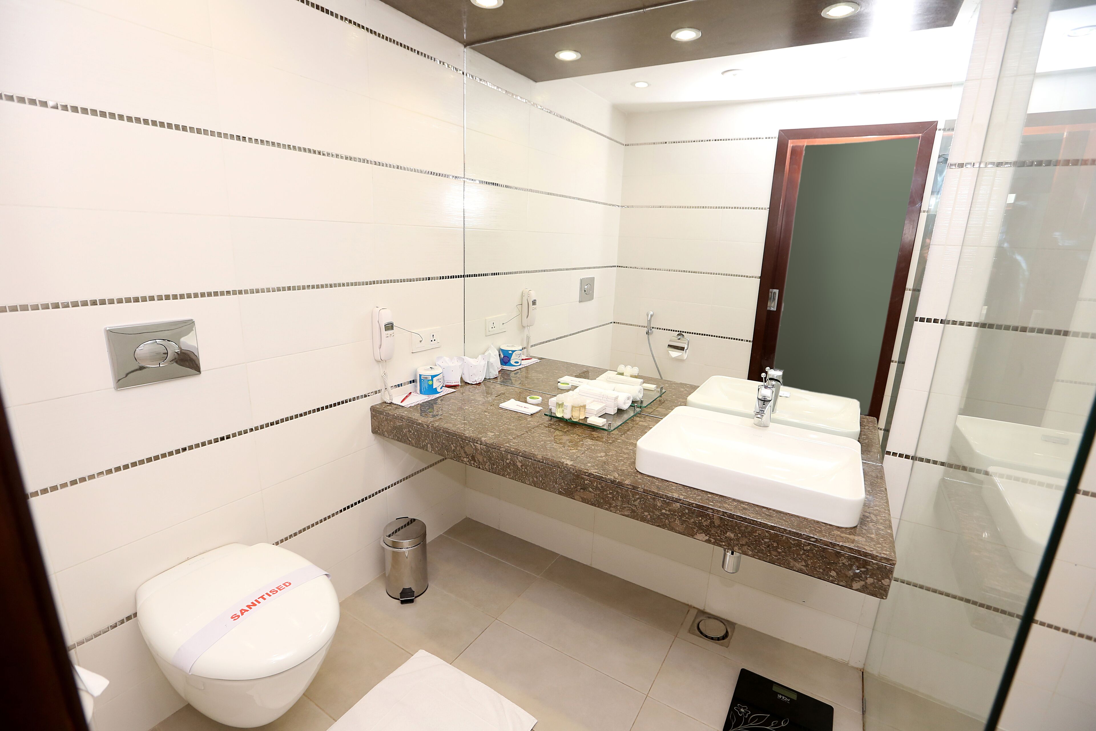 Un baño moderno con inodoro, dos lavamanos, un espejo y un cubo de basura.