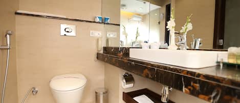 A modern bathroom with a white toilet, a shower, a sink with a marble countertop, and a mirror reflecting the room.