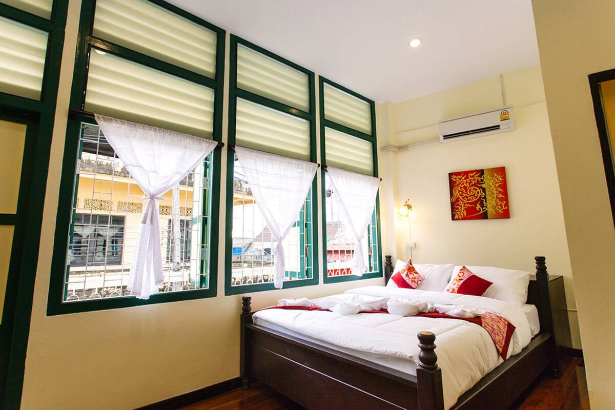 A bedroom with a large bed, a window with curtains, and a wall-mounted air conditioner.