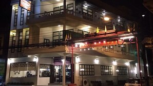 A multi-story hotel with balconies, a covered walkway, and a car parked in front. - Srisomboon Hostel (Trang)