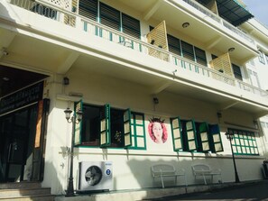 A two-story building with a balcony, a sign for a hotel, and a large air conditioning unit on the ground floor. - Srisomboon Hostel (Trang)