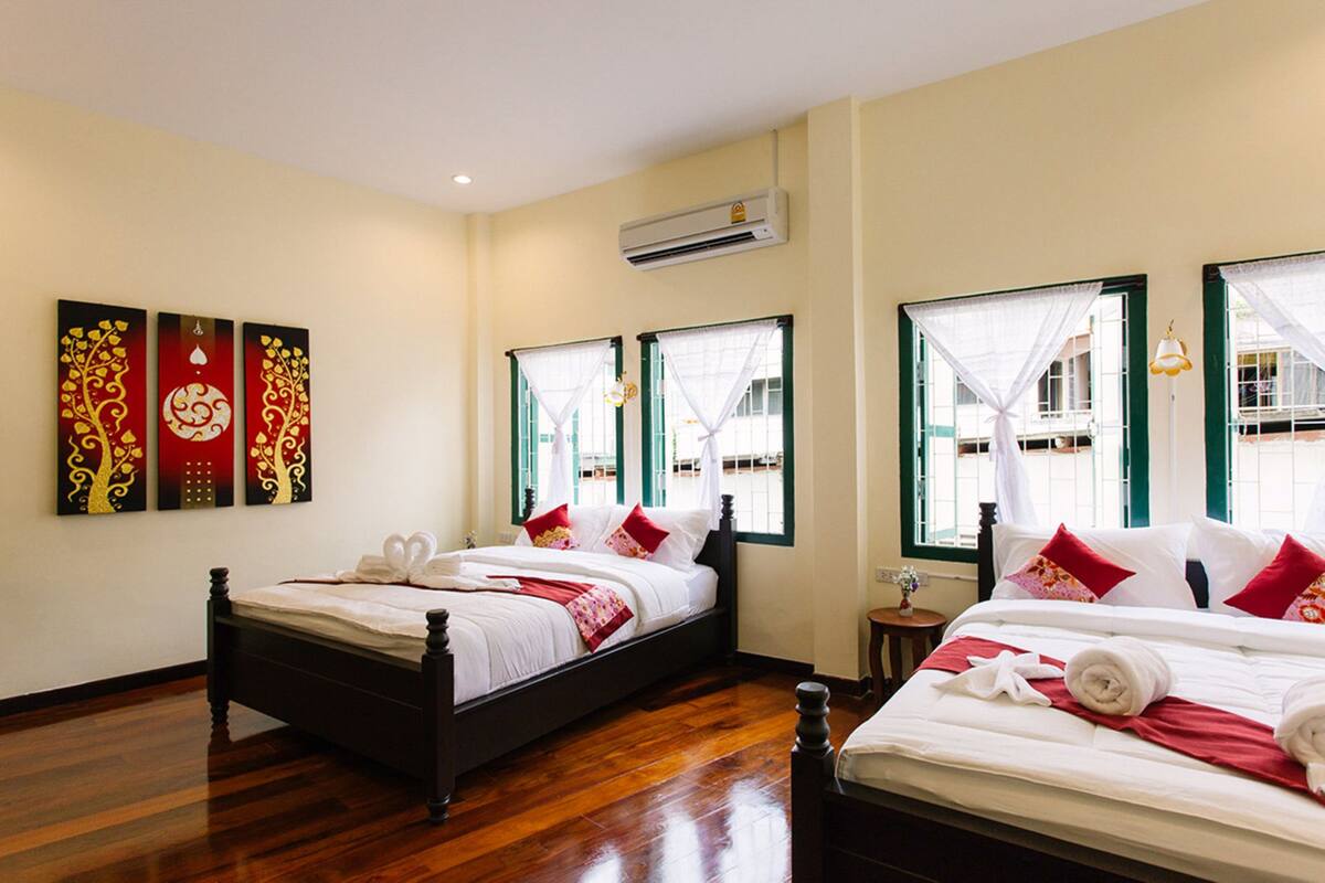 A hotel room with two beds, wooden flooring, a wall-mounted air conditioner, and decorative wall art.