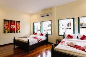 A hotel room with two beds, wooden flooring, a wall-mounted air conditioner, and decorative wall art. - Srisomboon Hostel (Trang)