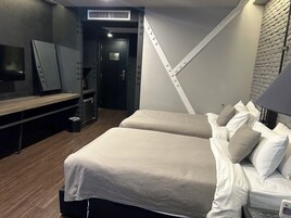 Una habitación de hotel moderna con dos camas, un escritorio, un espejo y una pared de ladrillo.