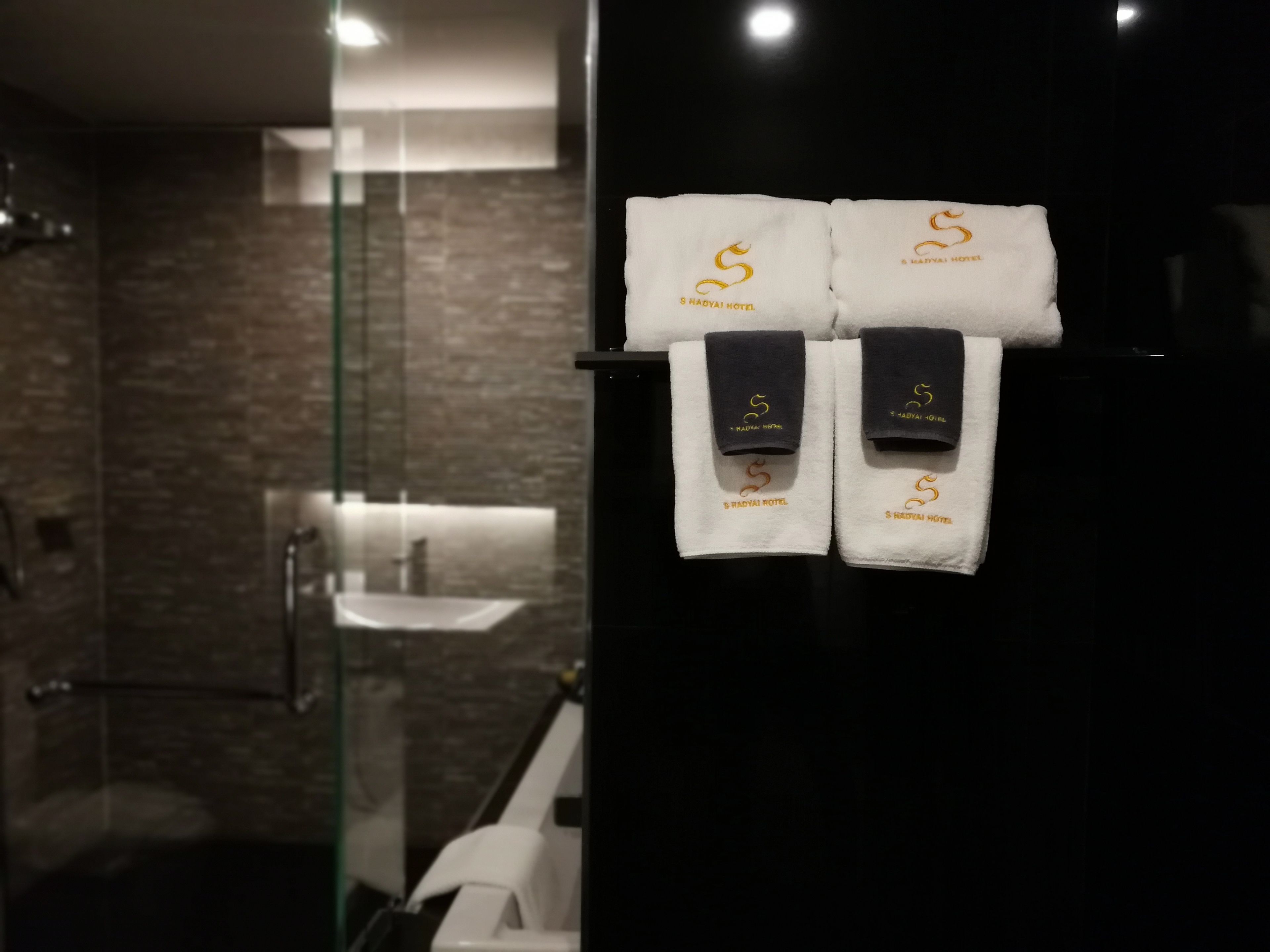 A bathroom with a glass shower enclosure, a sink, and towels hanging on a rack.