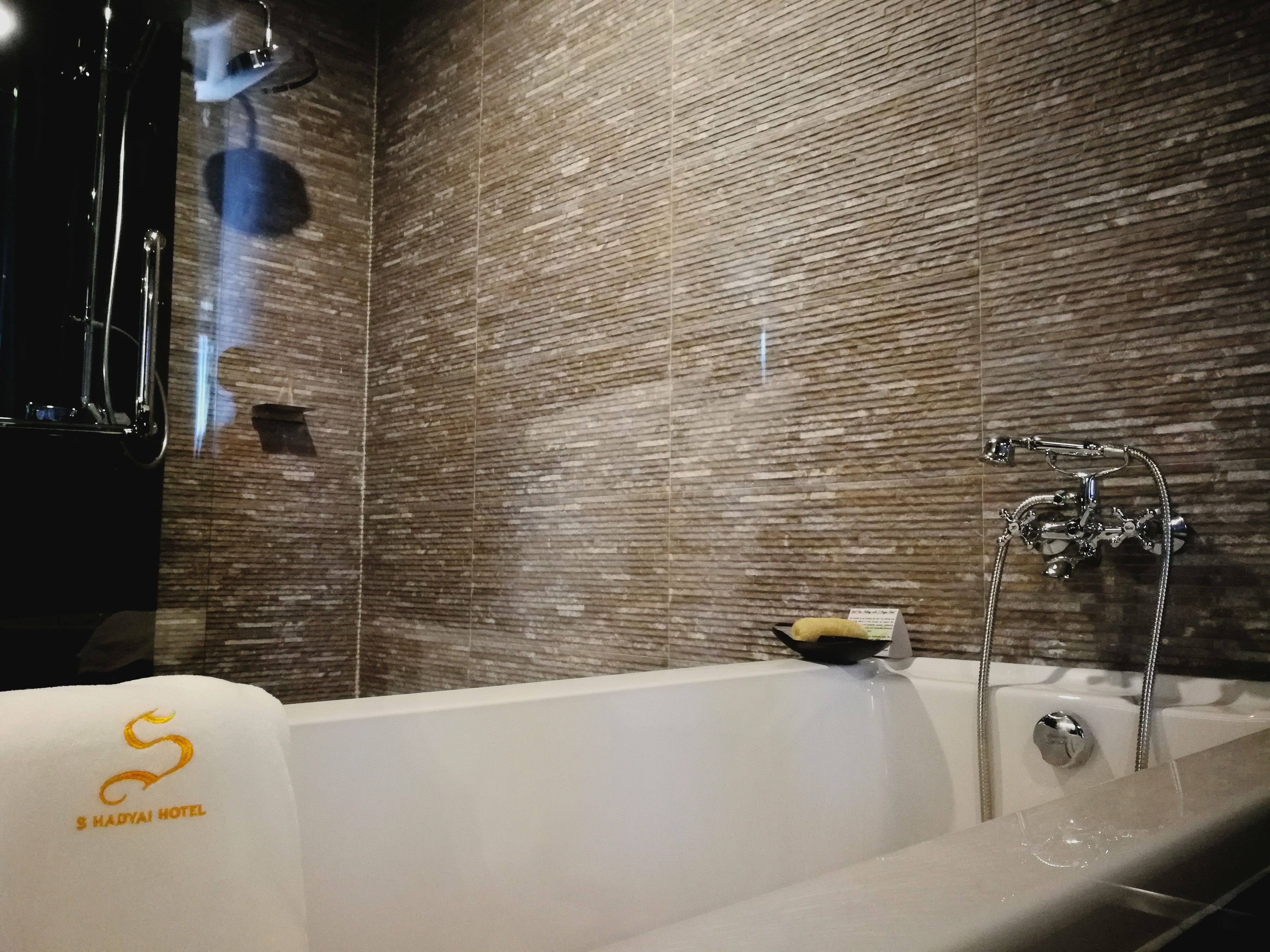 A modern bathroom with a bathtub, a shower, and a textured wall.