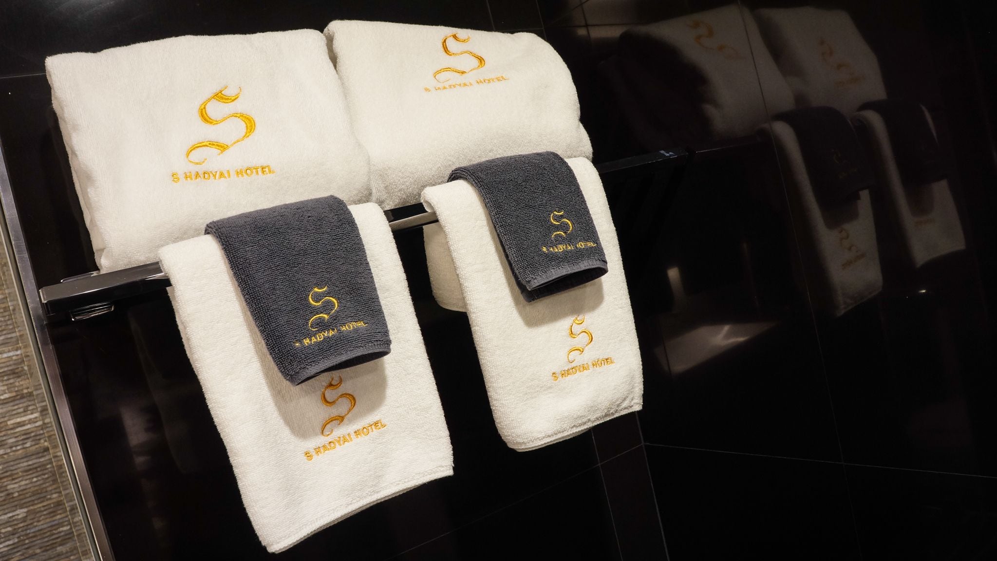 A set of towels with the logo of Shadyai Hotel on a black-tiled wall.