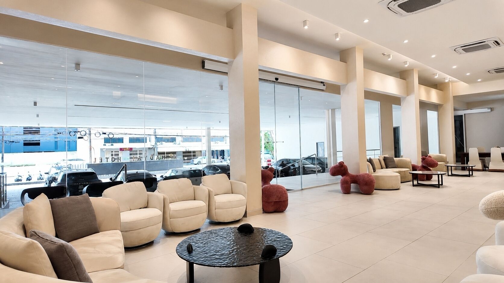 A modern hotel lobby with seating areas, large windows, and a view of the street.