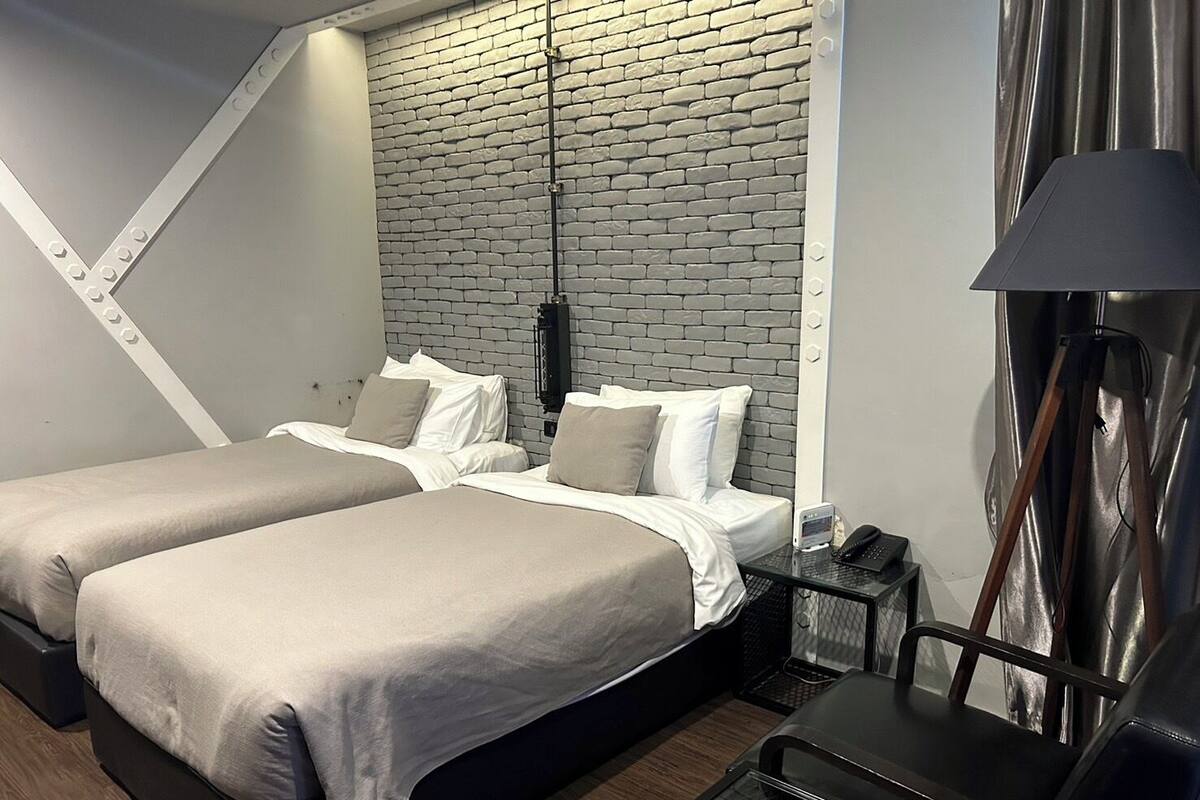 A modern hotel room with two beds, a brick-patterned headboard, a desk with a lamp, and a telephone.