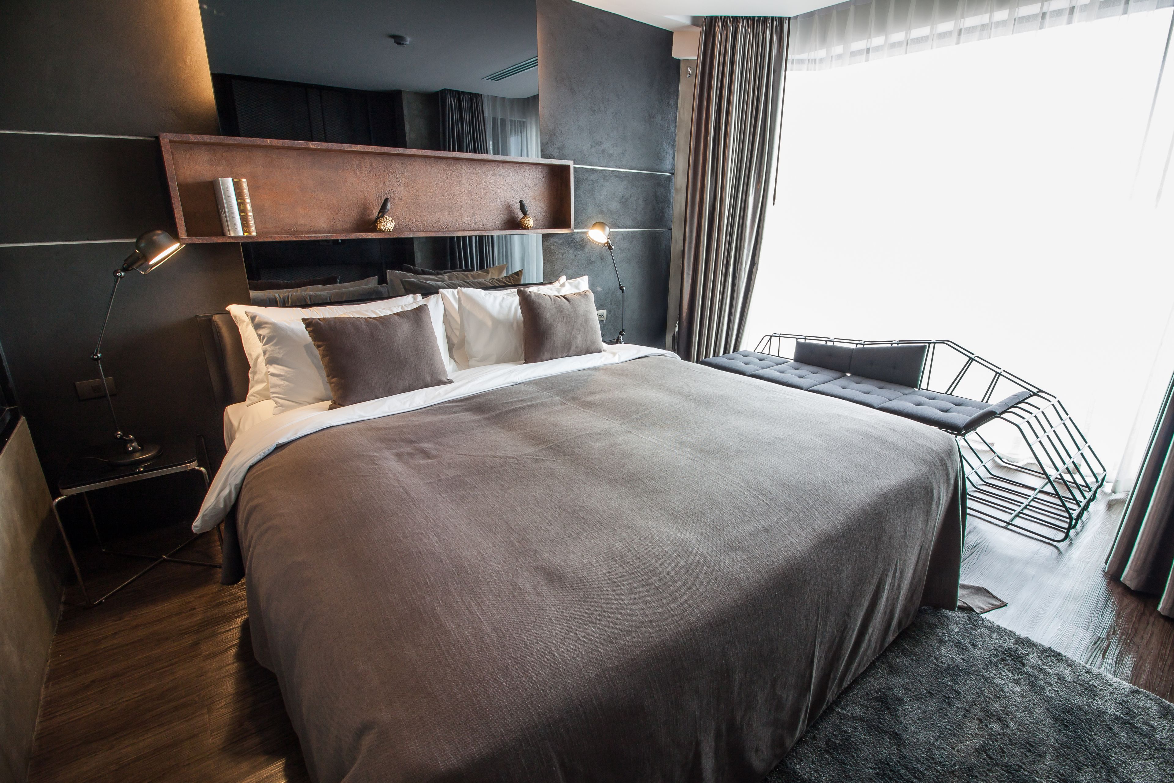 A modern bedroom with a large bed, bedside lamps, a wooden shelf, and a view of the outdoors.