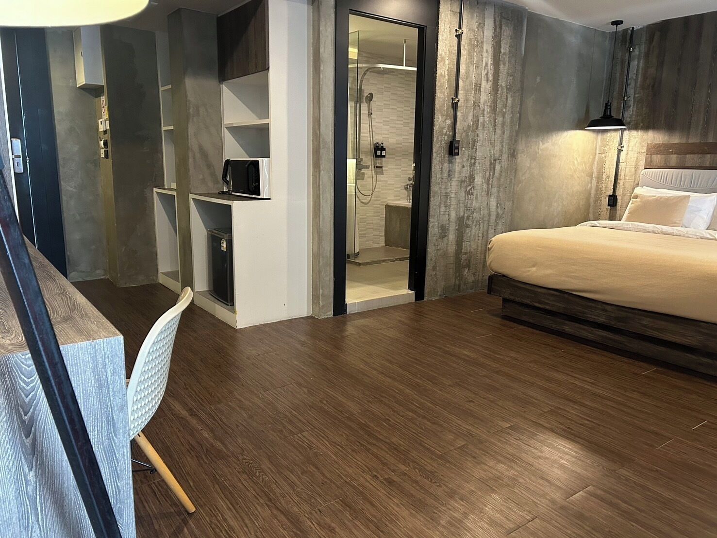 A modern bedroom with a wooden floor, a bed with white bedding, a desk with a chair, and a walk-in closet.