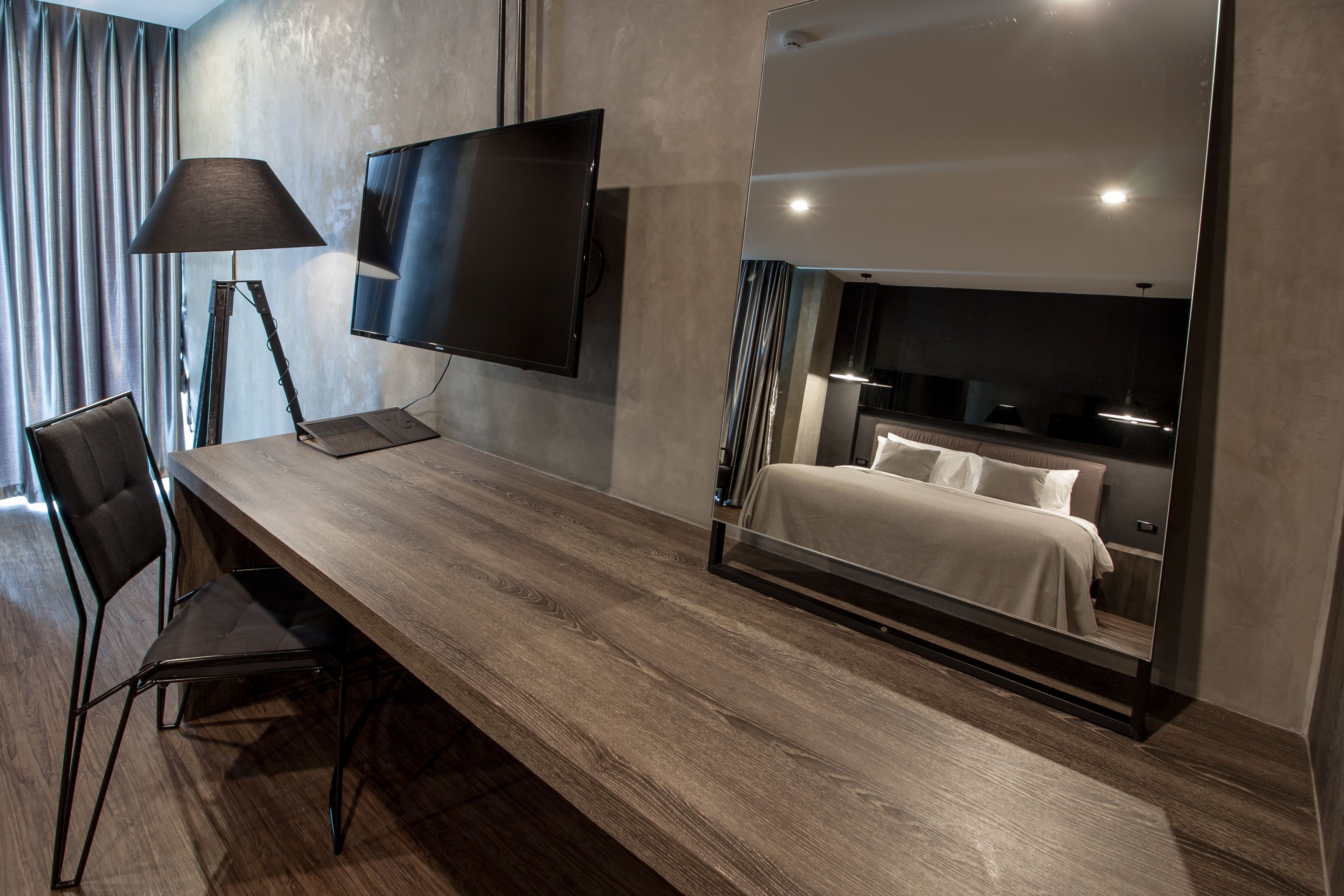 Een moderne hotelkamer met een houten bureau, een flatscreen televisie, een stoel, een bed met hoofdeinde en een grote spiegel.
