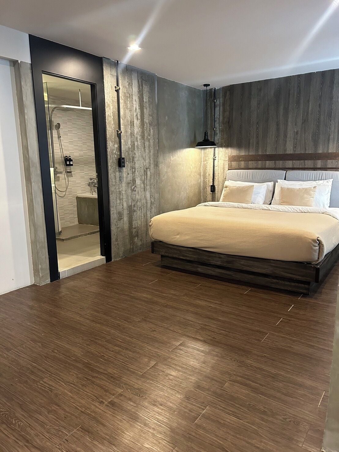 A modern bedroom with a large bed, a walk-in shower, and a wooden floor.