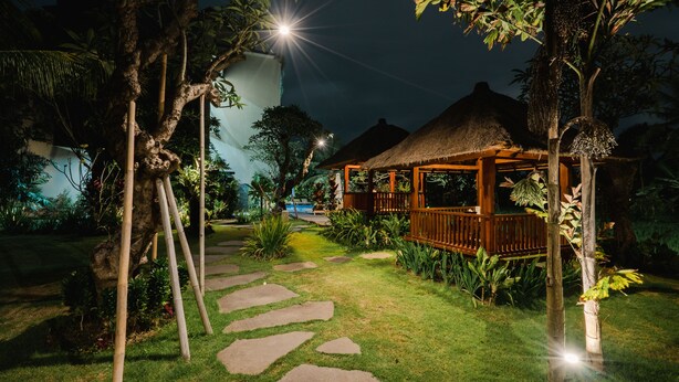 A nighttime garden with a thatched-roof gazebo, stone pathways, and tropical vegetation. - Byasa Ubud (Ubud)