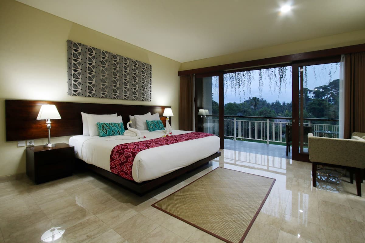 A hotel room with a large bed, two bedside tables with lamps, a decorative wall piece, a balcony with a view, and a chair.