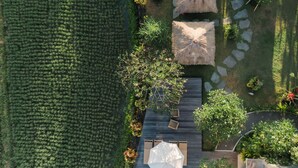 An aerial view of a landscaped garden with a wooden deck, stone pathway, and thatched umbrellas. - Byasa Ubud (Ubud)