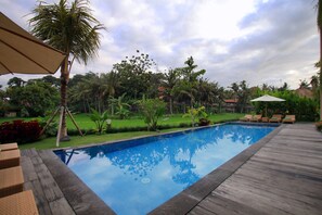 Relax by the serene pool surrounded by lush greenery and palm trees.