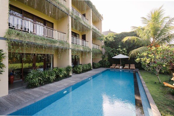 Un hotel con piscina, mobiliario exterior y abundante vegetación.