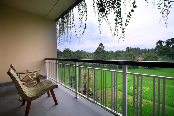 Un balcon avec une chaise et une table en osier, donnant sur un paysage verdoyant, avec des arbres et un ciel dégagé.