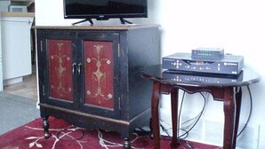 A television on a cabinet, a small table with electronic devices, and a red carpet. - Canora Cozy Cottage (Canora)