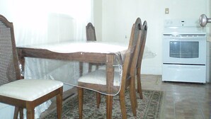 A dining area with a wooden table and chairs, a kitchen with an oven, and a patterned rug on the floor. - Canora Cozy Cottage (Canora)