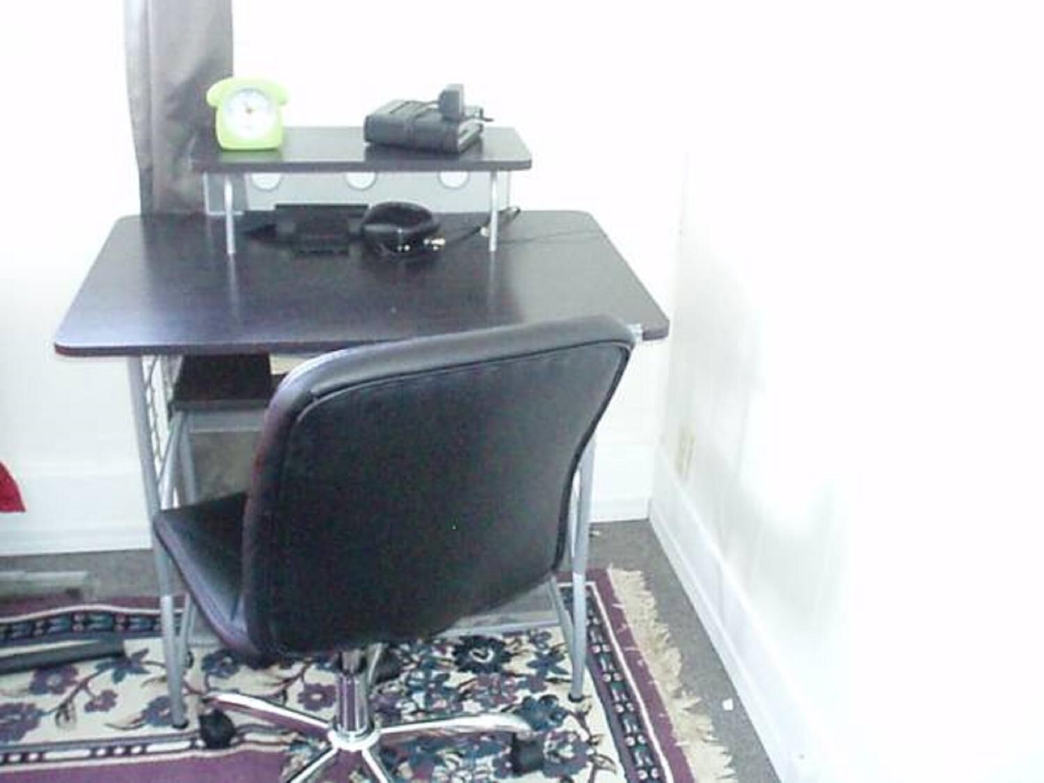 Ein kleiner Büroraum mit einem schwarzen Schreibtisch, einem Stuhl, einem Drucker und einem Telefon.
