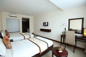 A hotel room with two beds, a desk, a chair, a TV, and a small table with flowers.