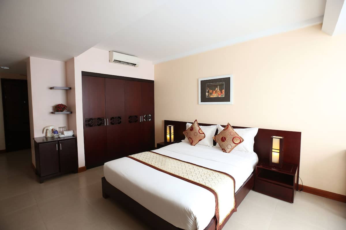 A hotel room with a large bed, a wardrobe, a bedside table with a lamp, and a picture on the wall.