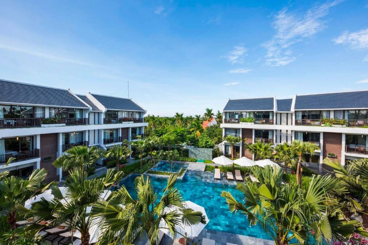 A resort with a central swimming pool surrounded by lush greenery and multiple hotel buildings with balconies.