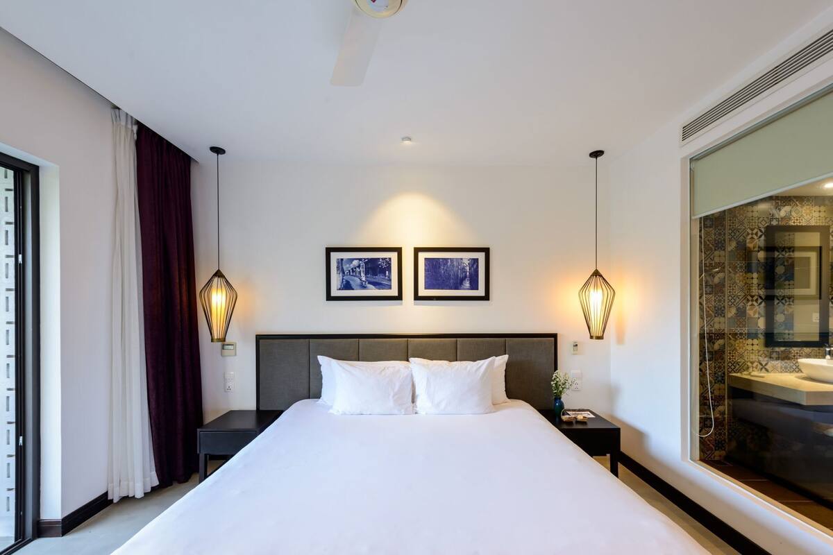 A hotel room with a large bed, two wall-mounted picture frames, a nightstand, a bedside table, and a large mirror.