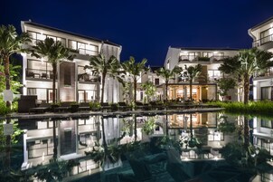 Un hotel moderno con varios balcones, piscina y abundante vegetación.