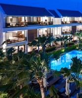 Un hotel moderno con piscina rodeada de palmeras y zonas de descanso.