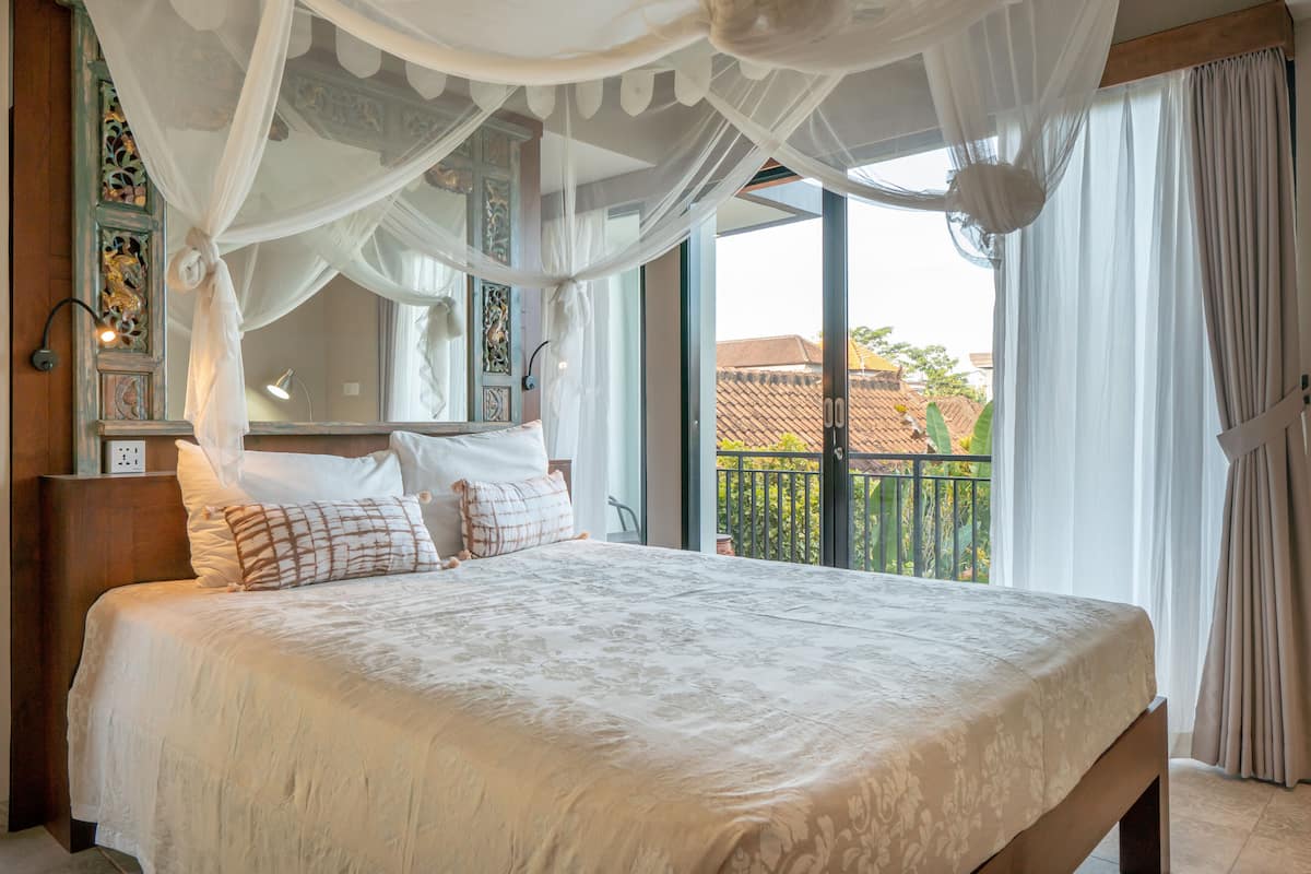 A bedroom with a large bed, a canopy, and a view of the outside.