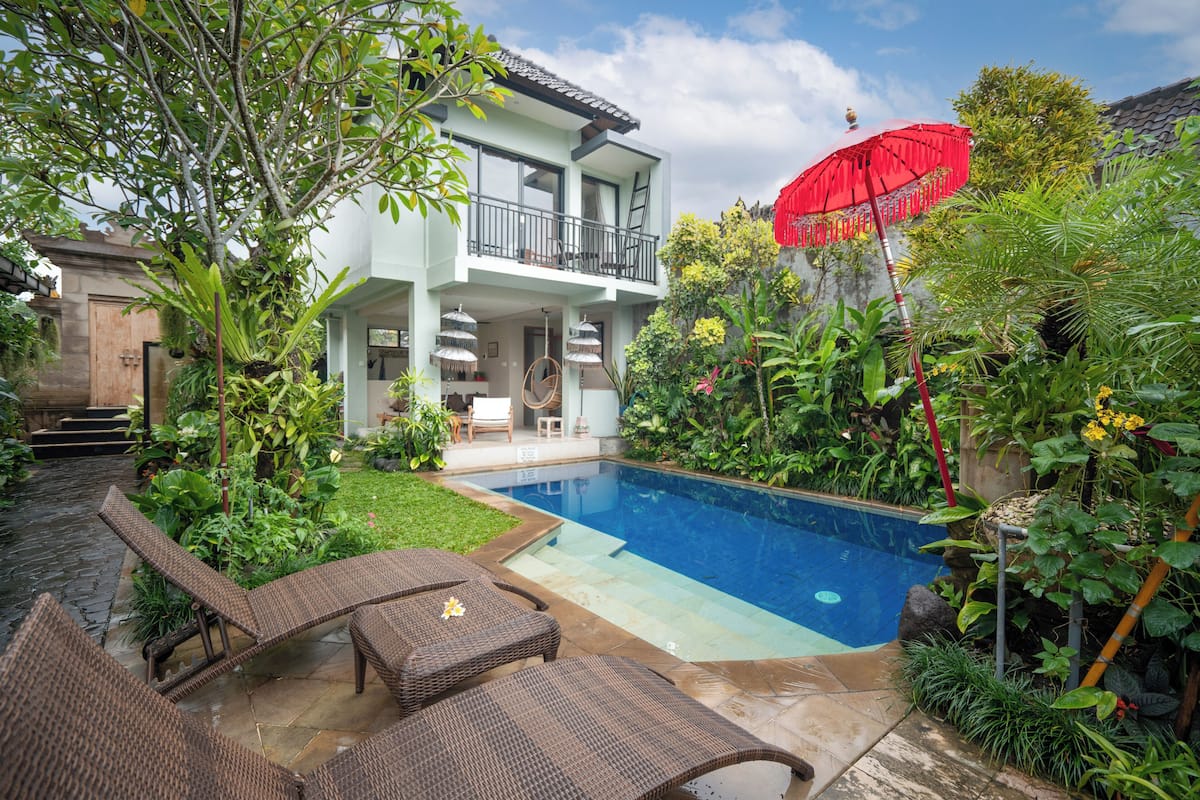 Una casa de dos pisos con piscina, mobiliario exterior y abundante vegetación.