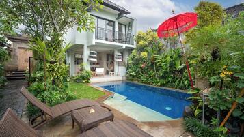 A two-story house with a swimming pool, outdoor furniture, and lush greenery.