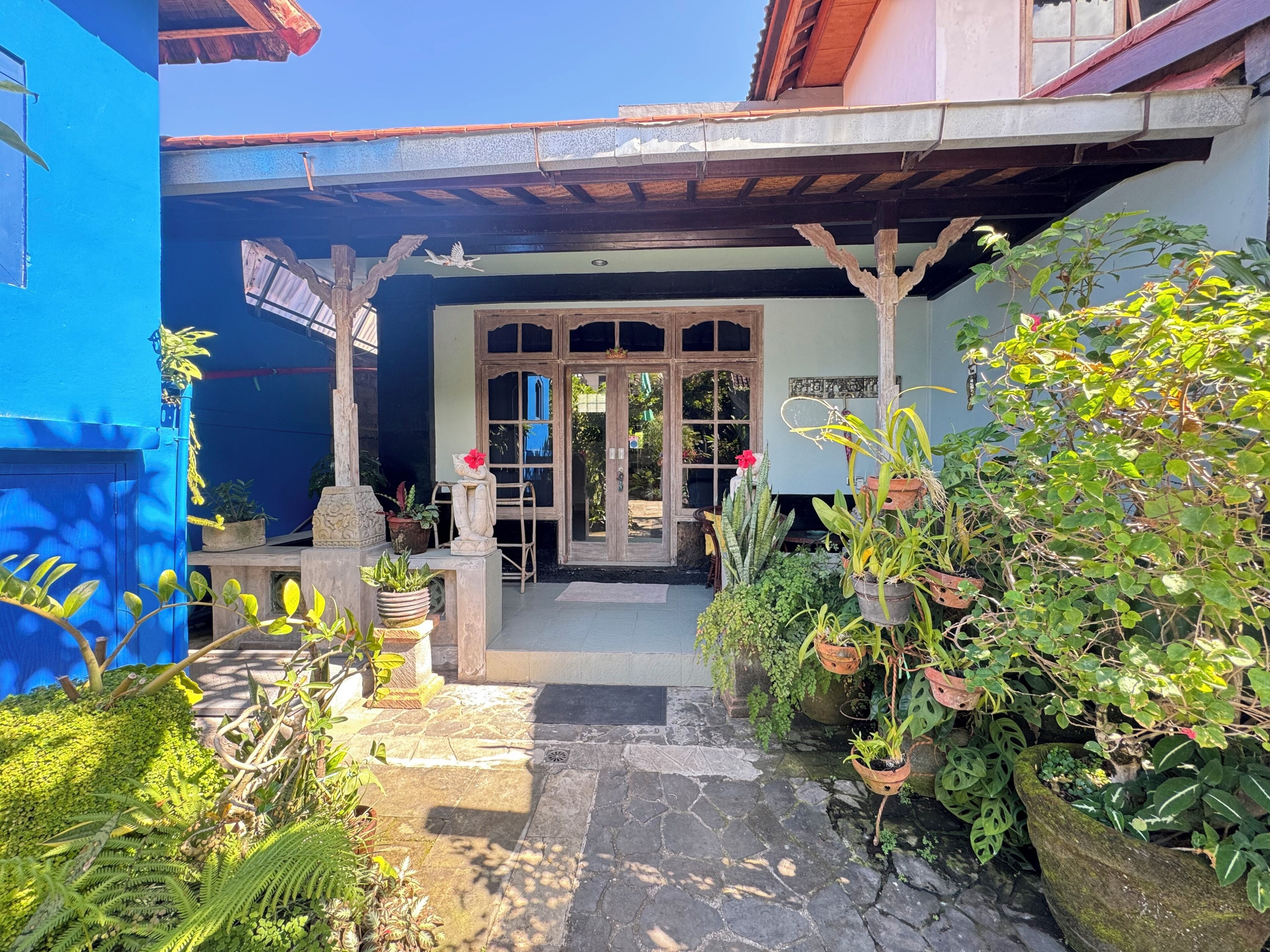 Un patio con un edificio azul, una pérgola de madera y plantas en macetas.