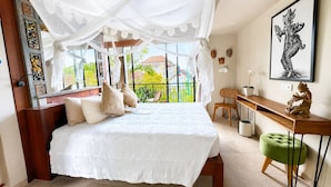 A bedroom with a large bed, a desk, a chair, and a balcony with a view. - Angel House Ubud Eco Villa (Mas)